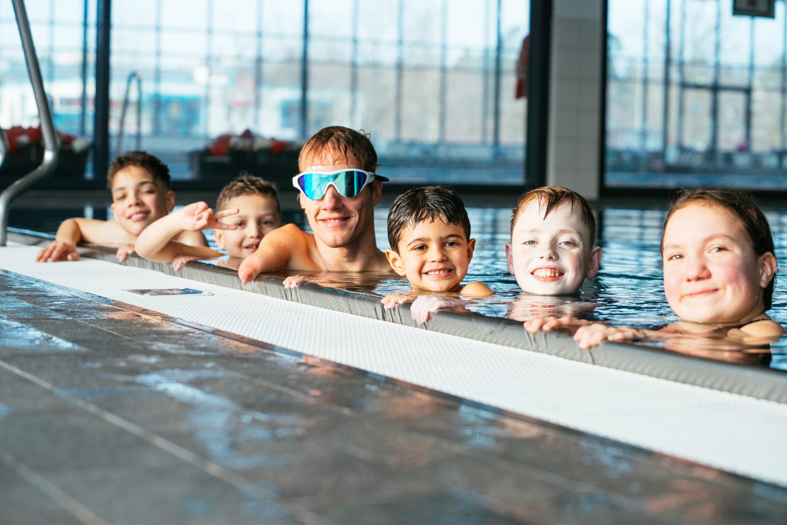 Eine Schwimmlehrerin und ein Kind mit Schwimmnudel lachen gemeinsam im Wasser